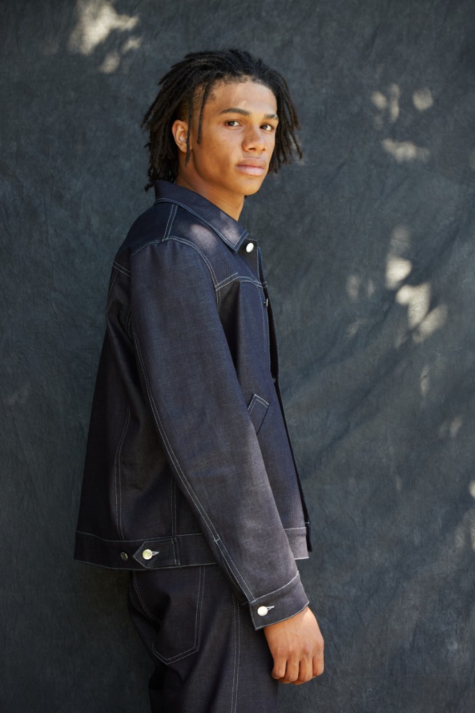 Modeling portrait of Nnamdi Unamadu in dark denim against a textured grey backdrop